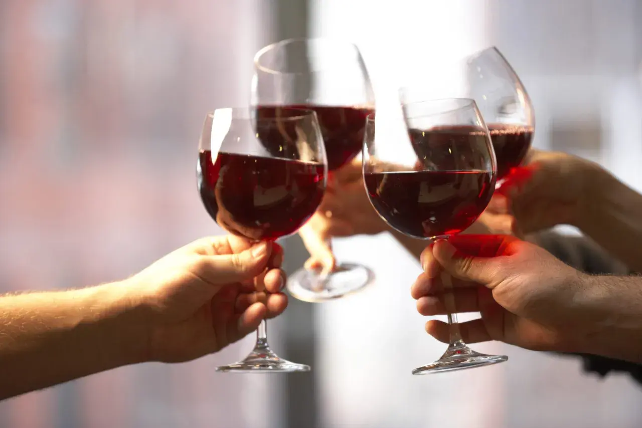 Quatre mains portent des verres de vin rouge pour un toast. Une belle façon de célébrer et de savoir comment boire du vin rouge.