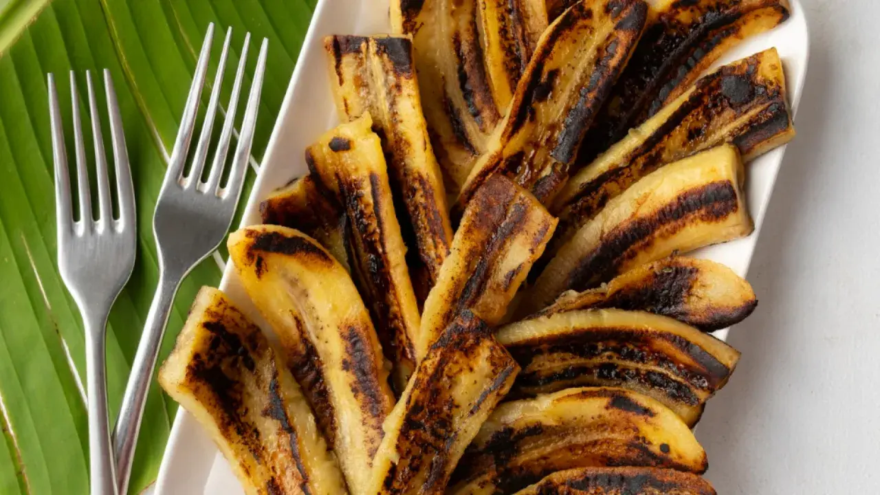 Bananes flambées grillées sur une feuille de bananier, prêtes à être dégustées avec deux fourchettes.