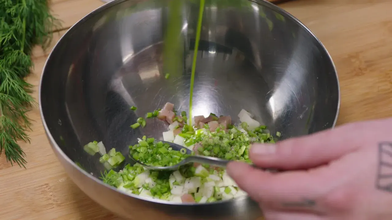Préparation d'une salade nordique : on verse une sauce verte sur des dés de poisson, oignons et aneth dans un bol.