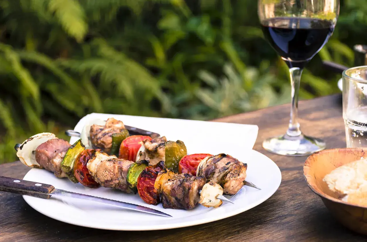 Brochettes de viande et légumes grillés, accompagnées d'un verre de vin pour grillade et d'un bol de pain.