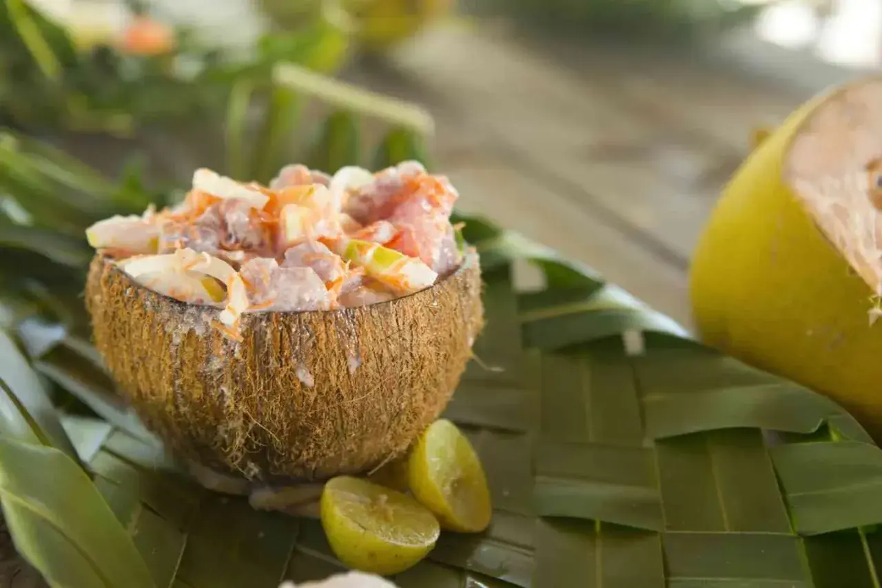 Salade tahitienne crémeuse servie dans une noix de coco, garnie de citron vert et de feuilles de palmier.
