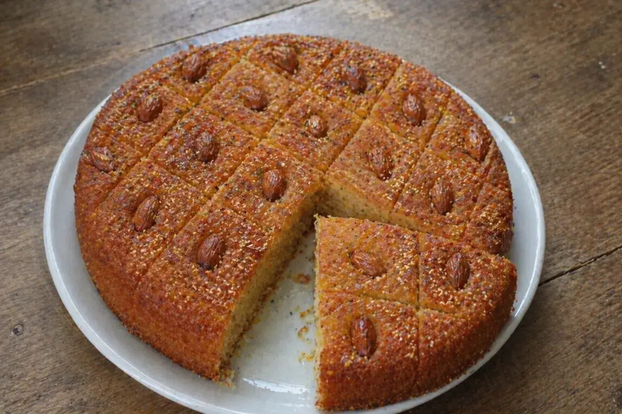Un délicieux gâteau arabe au miel, parsemé d'amandes et de graines, coupé en carrés sur une assiette blanche.