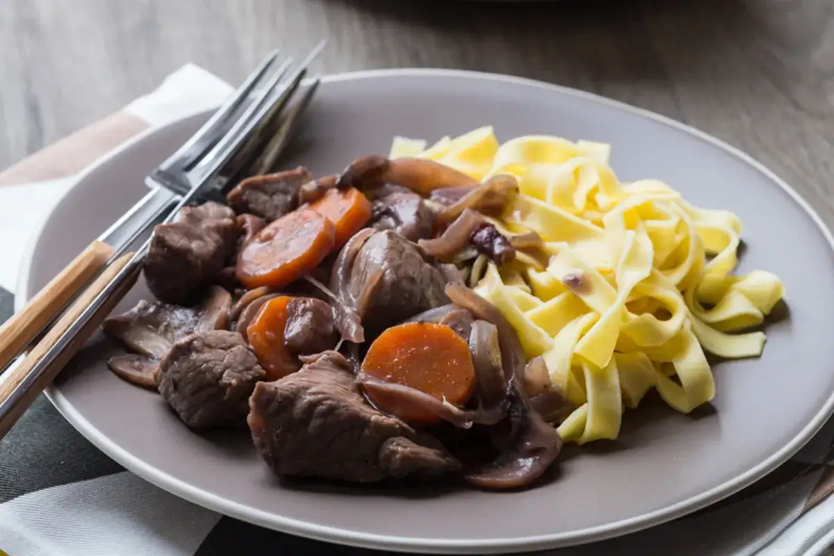 Un plat de bœuf bourguignon, carottes et champignons, servi avec des tagliatelles. Une recette cocotte minute SEB pour un repas savoureux.
