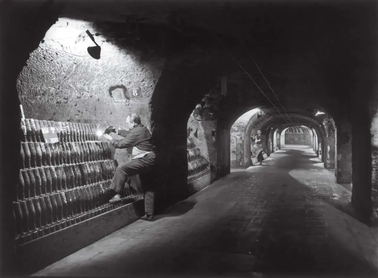 Dans une cave voûtée, un homme manipule des bouteilles, une étape clé de l'histoire du champagne.
