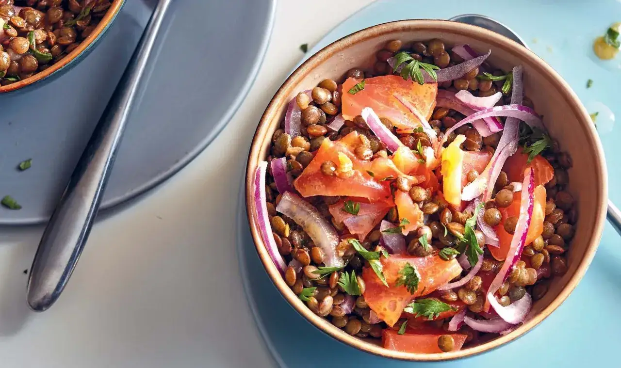 Salade de lentilles savoureuse avec des morceaux de saumon, des oignons rouges et du persil frais. Un plat coloré et nutritif.