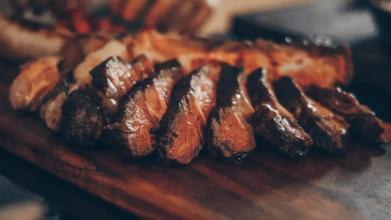 Tranches de viande grillée sur une planche en bois. Quel vin avec une pierrade ? Un rouge corsé comme un Syrah ou un Cabernet Sauvignon serait parfait.