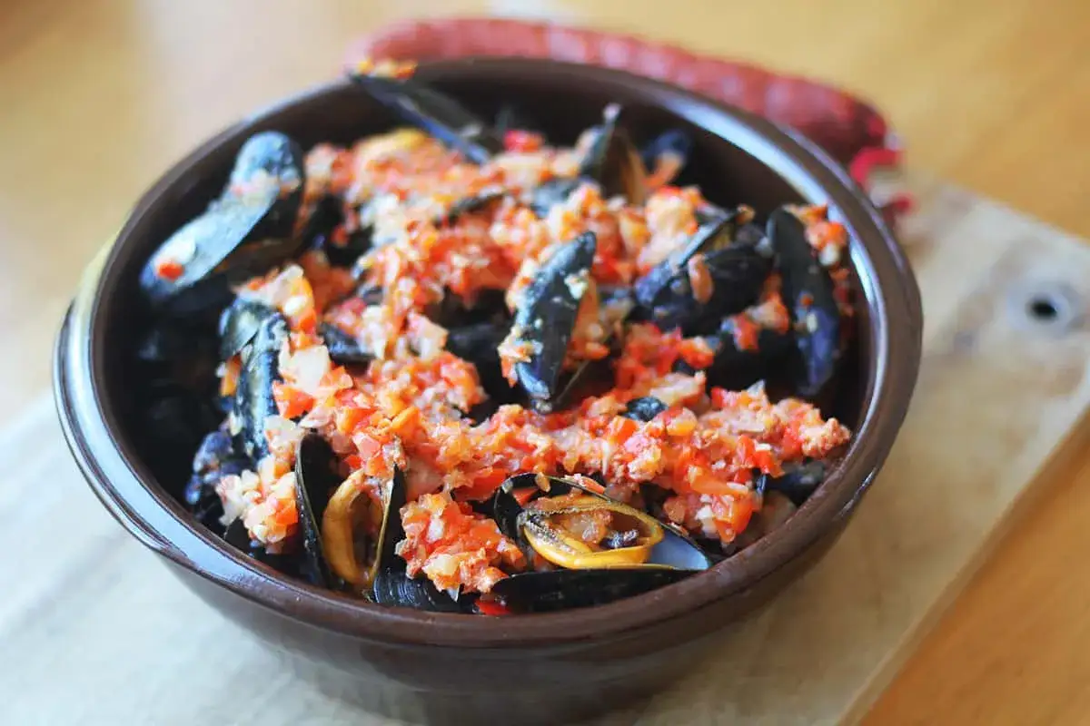 Un bol de moules au chorizo, garnies d'une sauce tomate et poivrons rouges, prêtes à être dégustées.
