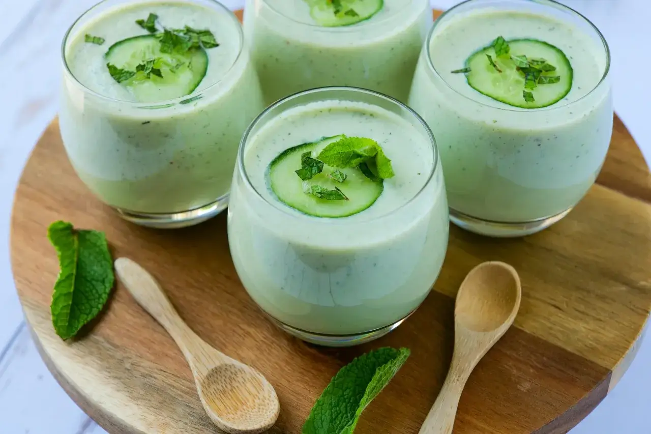 Quatre verres de gaspacho concombre frais, d&eacute;cor&eacute;s de rondelles de concombre et de menthe, sur un plateau en bois avec des cuill&egrave;res.