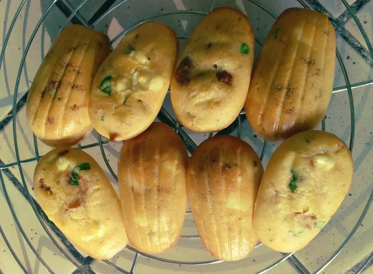 Huit madeleines sal&eacute;es, dor&eacute;es et moelleuses, garnies de fromage et d'herbes, refroidissent sur une grille.