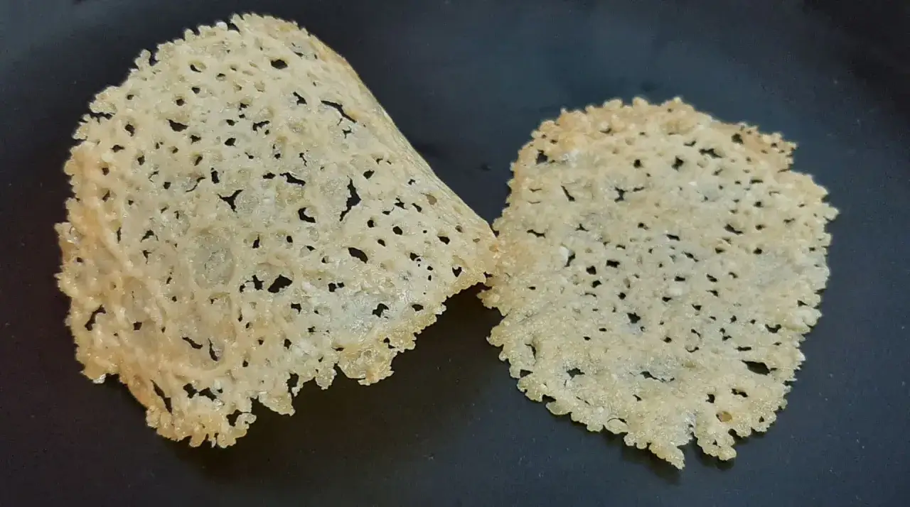 Deux tuiles de parmesan croustillantes et ajourées, posées sur une surface sombre.