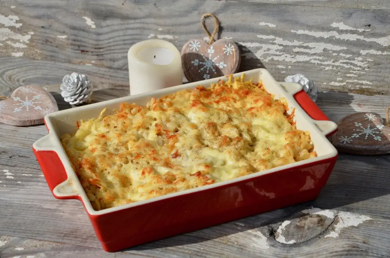 Un plat de gratin de crozet tout juste sorti du four, doré et gratiné, sur une table en bois rustique, décoré pour Noël.