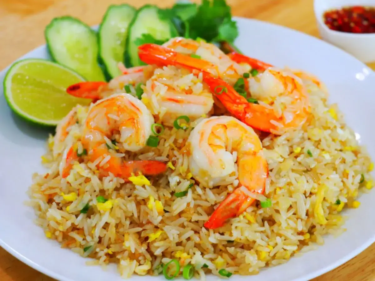 Un plat appétissant de riz frit thaï aux crevettes, garni de quartiers de citron vert, de concombre et de coriandre.
