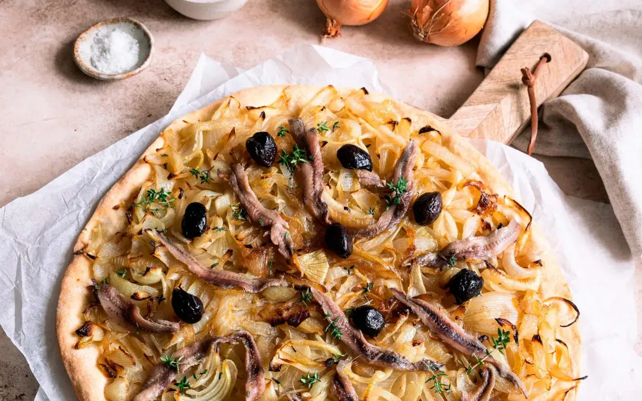 Pissaladière sur pâte brisée ou feuilletée, garnie d'oignons caramélisés, d'anchois et d'olives noires. Un délice méditerranéen.