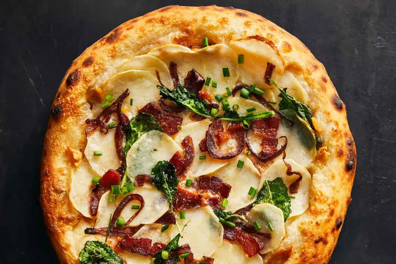 Pizza gourmande avec une base crémeuse, garnie de fines tranches de pommes de terre, lardons croustillants, oignons caramélisés et ciboule fraîche.