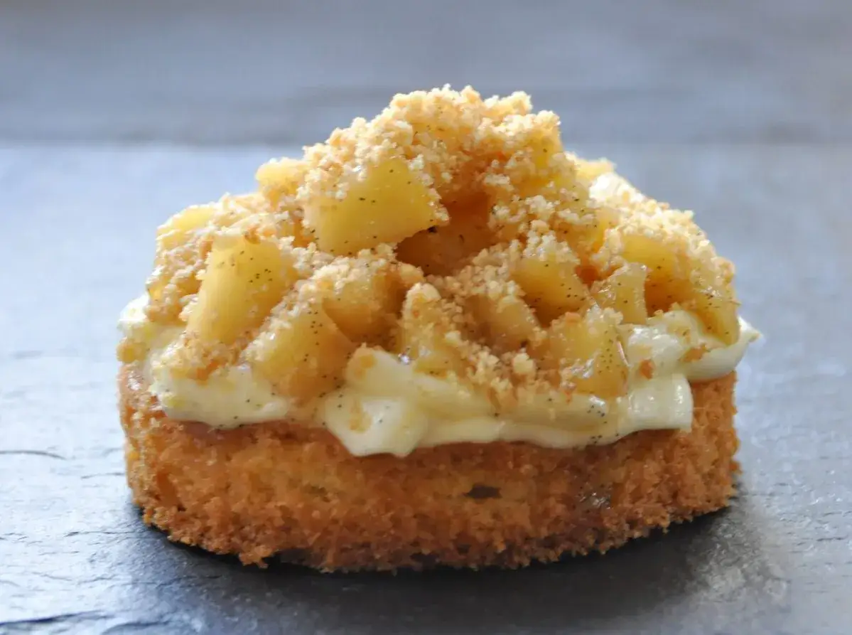 Gâteau breton individuel garni de pommes caramélisées, de crème vanillée et d'un crumble croustillant.