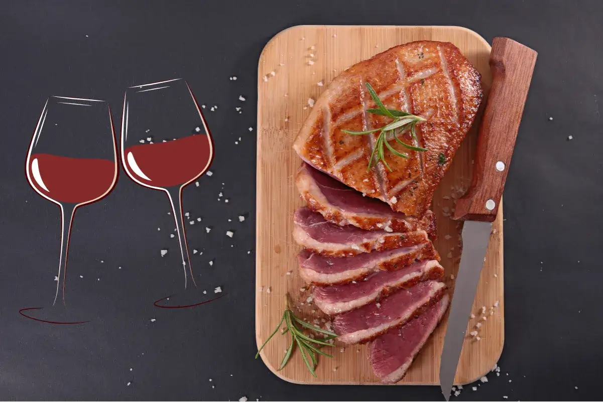 Un magret de canard tranch&eacute;, garni de romarin, pr&ecirc;t &agrave; &ecirc;tre d&eacute;gust&eacute; avec un verre de pinot noir.