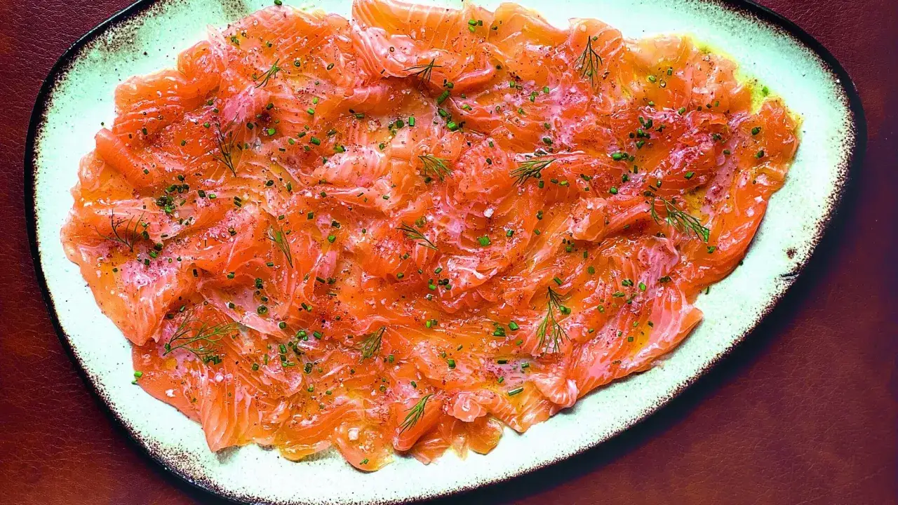 D&eacute;licieux carpaccio de saumon finement tranch&eacute;, parsem&eacute; d'aneth frais et de ciboulette, sur une assiette claire.