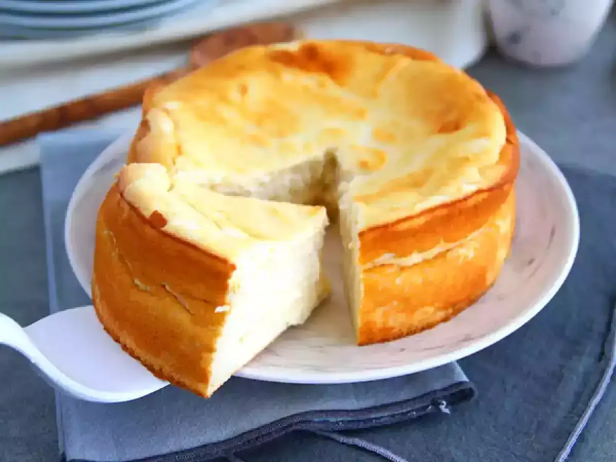 Un d&eacute;licieux g&acirc;teau au fromage blanc, dor&eacute; et moelleux, est servi sur une assiette blanche. Une part a &eacute;t&eacute; coup&eacute;e, r&eacute;v&eacute;lant sa texture a&eacute;rienne.