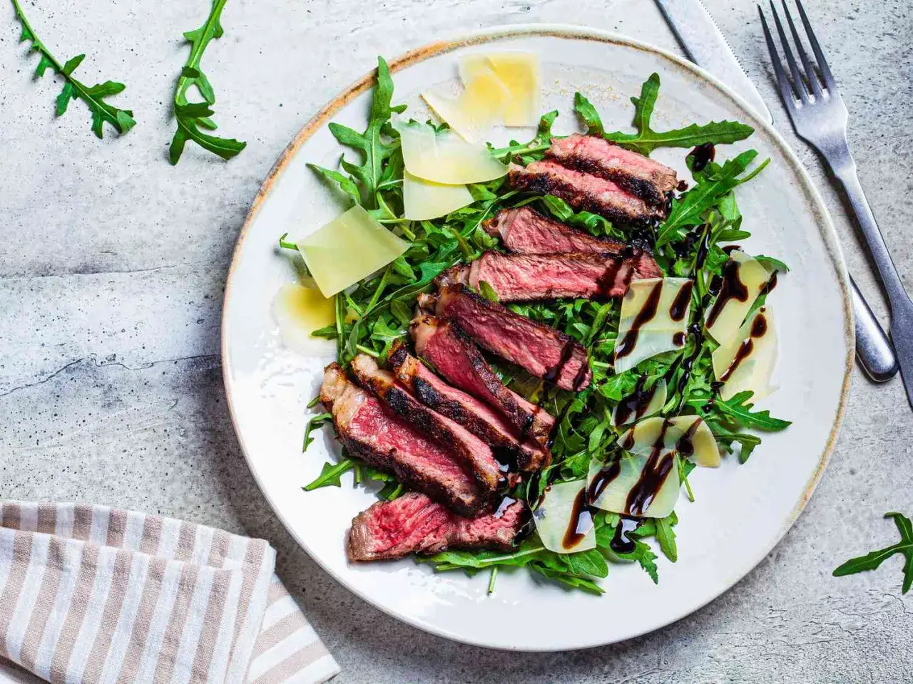 Une assiette de tagliata de boeuf, roquette, copeaux de parmesan et filet de vinaigre balsamique.