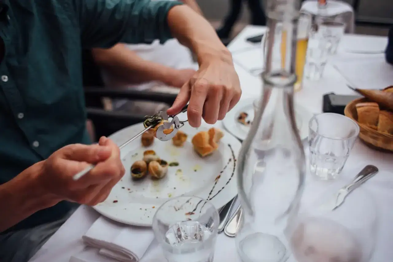 Un homme déguste des escargots, une question se pose : quel vin avec les escargots ? Une carafe d'eau et du pain sont sur la table.