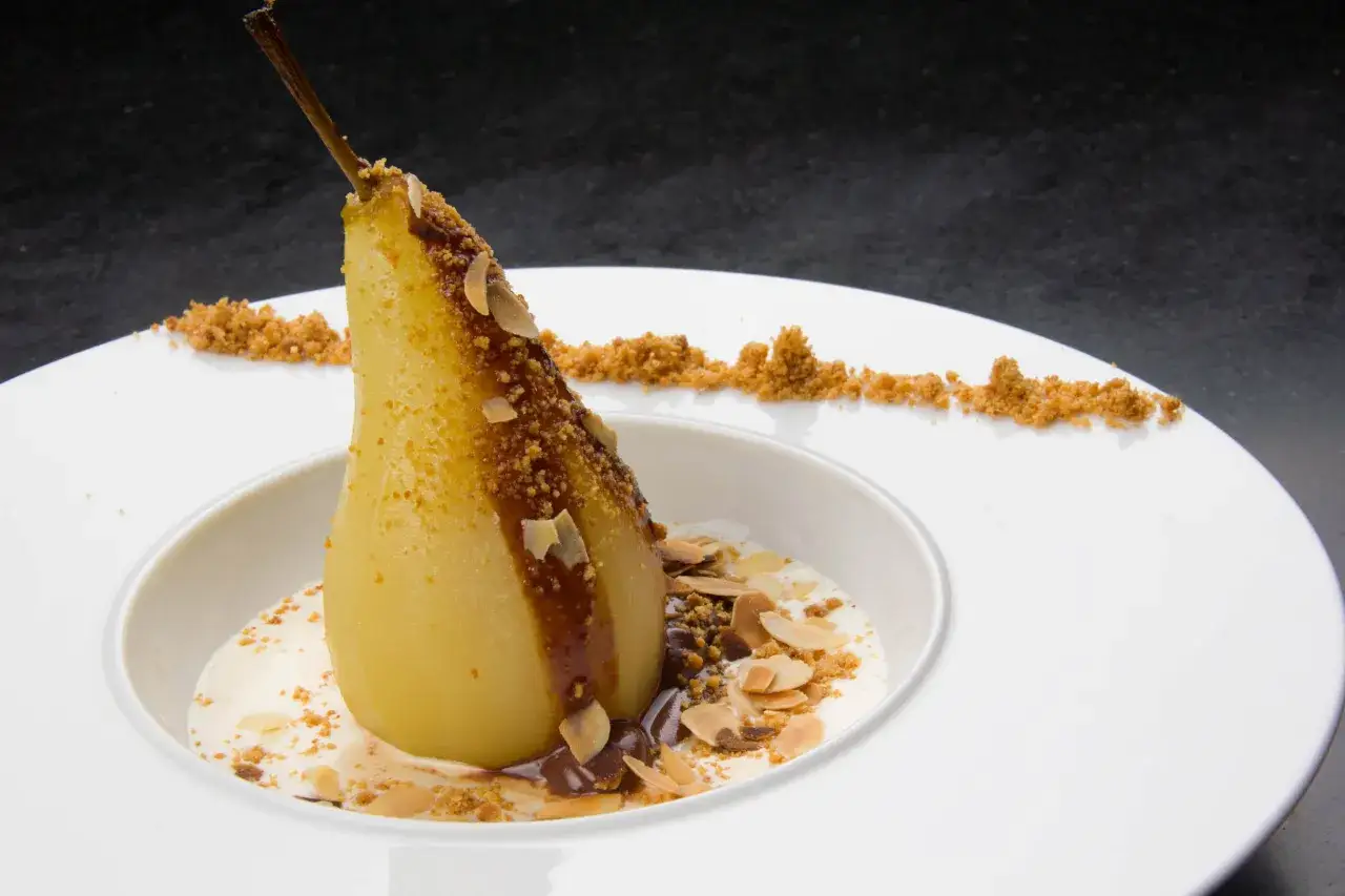 Une poire pochée, nappée de sauce au chocolat et parsemée d'amandes effilées, baigne dans une crème onctueuse. Un délice de poire belle Hélène.