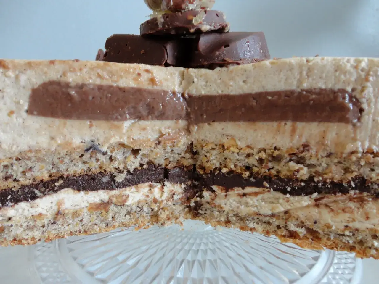Tranche d'un g&acirc;teau aux couches de mousse l&eacute;g&egrave;re et de ganache chocolat, sur une base de dacquoise noisette croustillante. D&eacute;cor&eacute; de morceaux de chocolat.