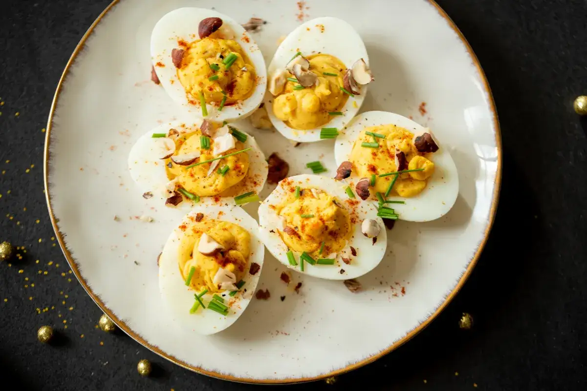 Six oeufs mimosa garnis de ciboulette et de noisettes concass&eacute;es, saupoudr&eacute;s de paprika, sur une assiette blanche bord&eacute;e d'or.