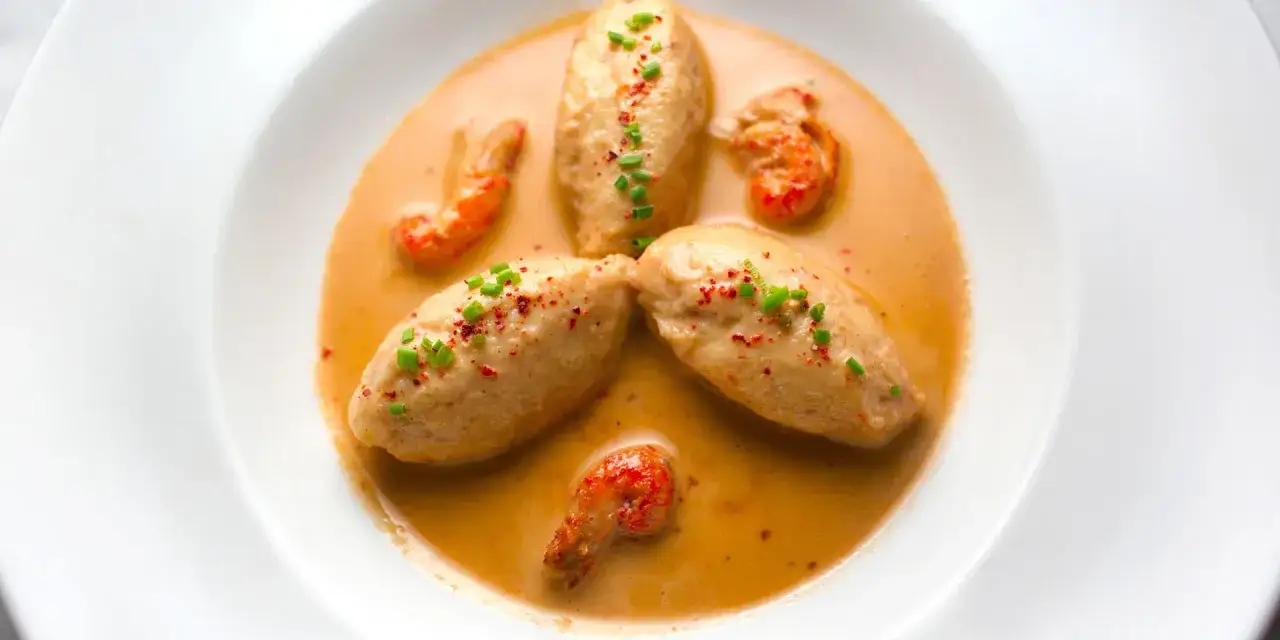 Quatre quenelles de brochet, garnies de ciboule et de paprika, nagent dans une sauce crémeuse avec des écrevisses.