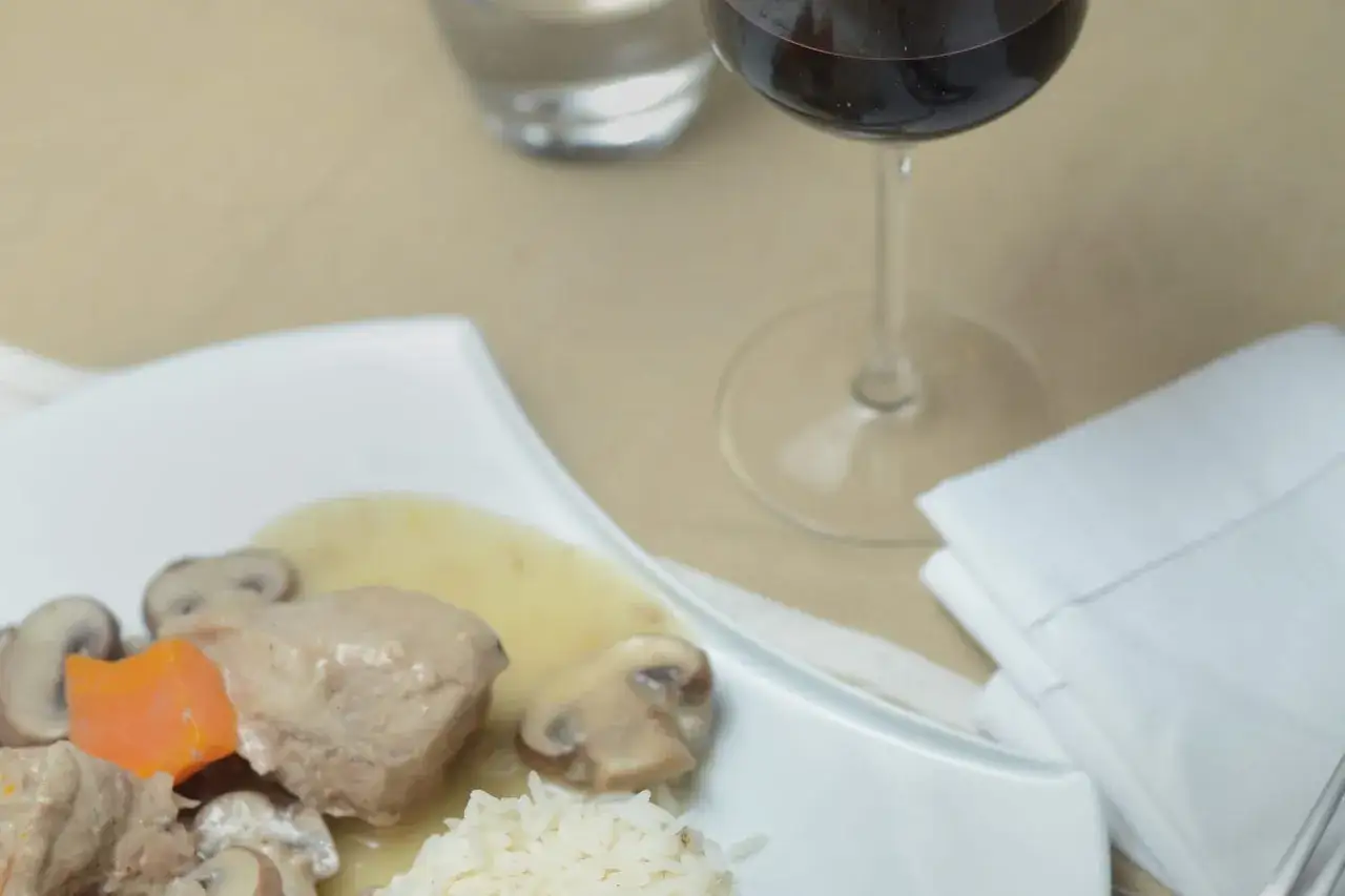 Un verre de vin rouge accompagne une blanquette de veau onctueuse avec riz et champignons.