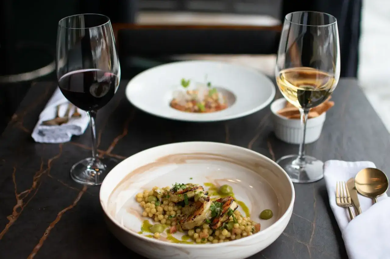 Deux verres de vin, l'un rouge, l'autre blanc, accompagnent des plats raffinés. Le vin blanc, avec sa touche de citron, promet une dégustation fraîche.