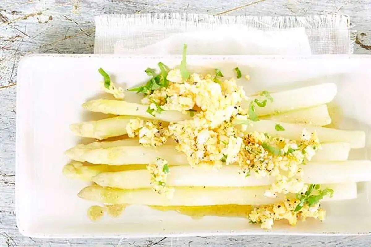 Asperges à la flamande : des asperges blanches tendres nappées d'une sauce aux œufs brouillés et herbes fraîches, un délice printanier.