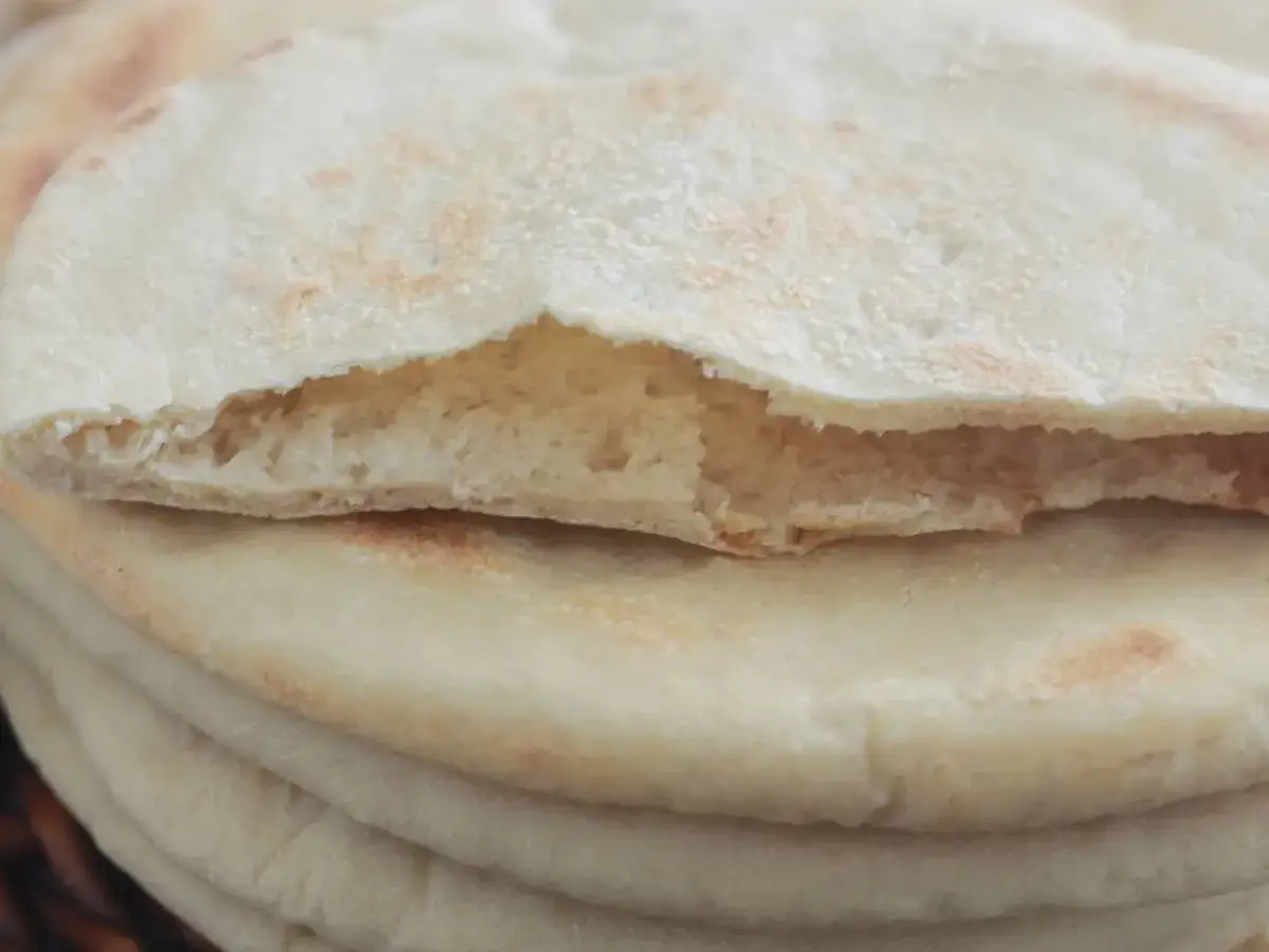 Une pile de pains pita moelleux, dont un est ouvert pour révéler sa texture aérée. Parfait pour garnir de vos ingrédients préférés.