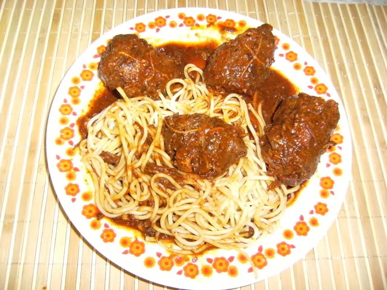 Un plat de spaghetti avec des ragoûts de bœuf en sauce, ressemblant à des alouettes sans tête, sur une assiette décorée de fleurs.