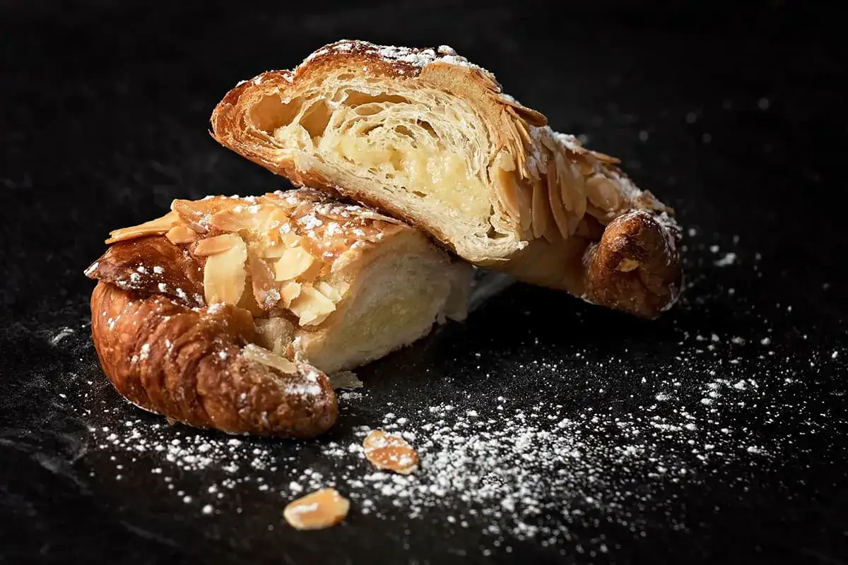 Un délicieux croissant aux amandes, saupoudré de sucre glace, révèle sa garniture crémeuse.