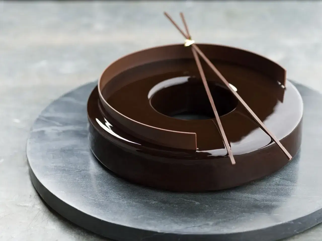Gâteau rond avec un glaçage chocolat miroir, décoré de fines lamelles de chocolat.