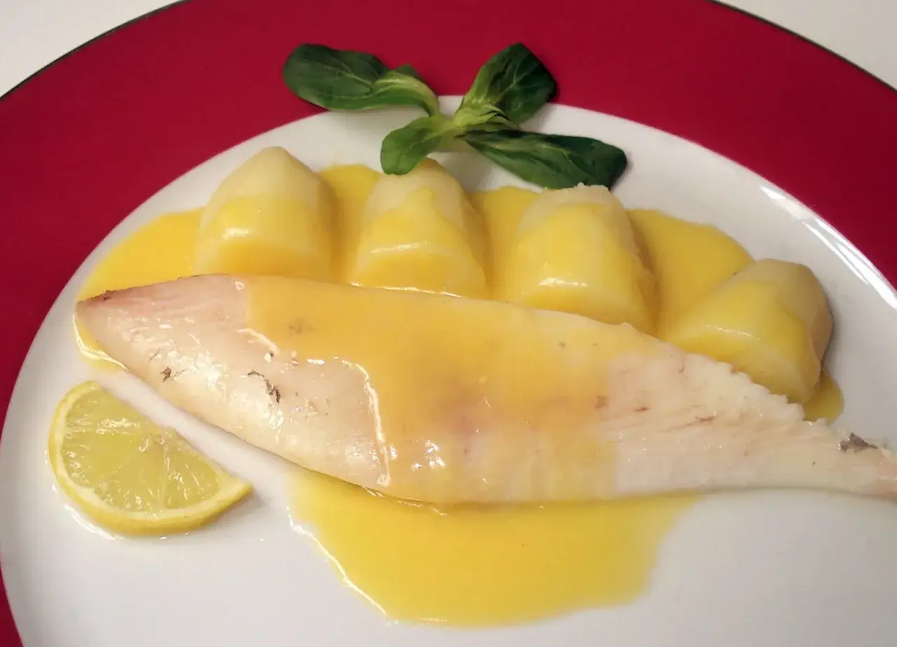 Un délicieux filet de saint pierre nappé d'une sauce hollandaise, accompagné de pommes de terre et d'une tranche de citron.