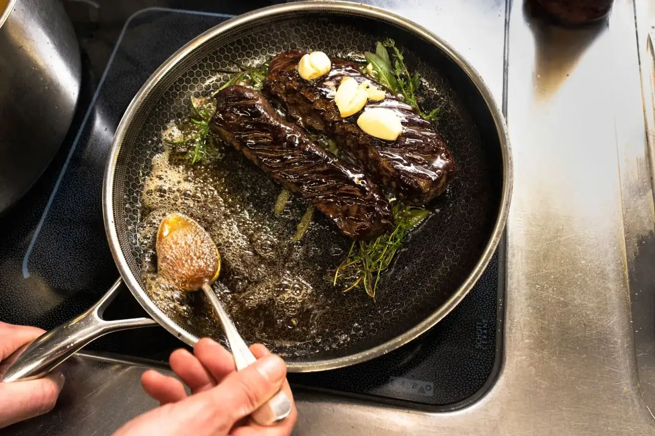 Deux onglets de bœuf poêlés avec ail et herbes, le jus de cuisson est arrosé à la cuillère. Une étape clé de la recette onglet de boeuf.