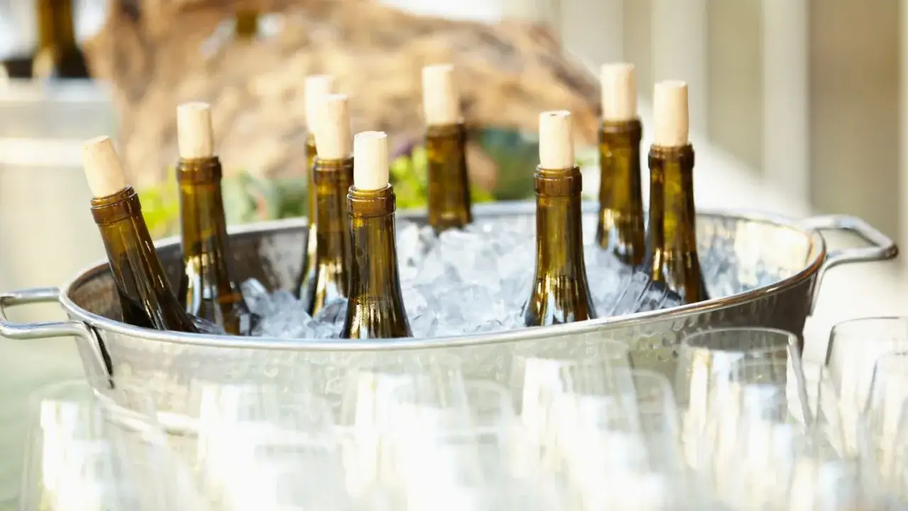 Bouteilles de vin dans un seau de glace pour refroidir une bouteille rapidement. Verres à pied flous au premier plan.