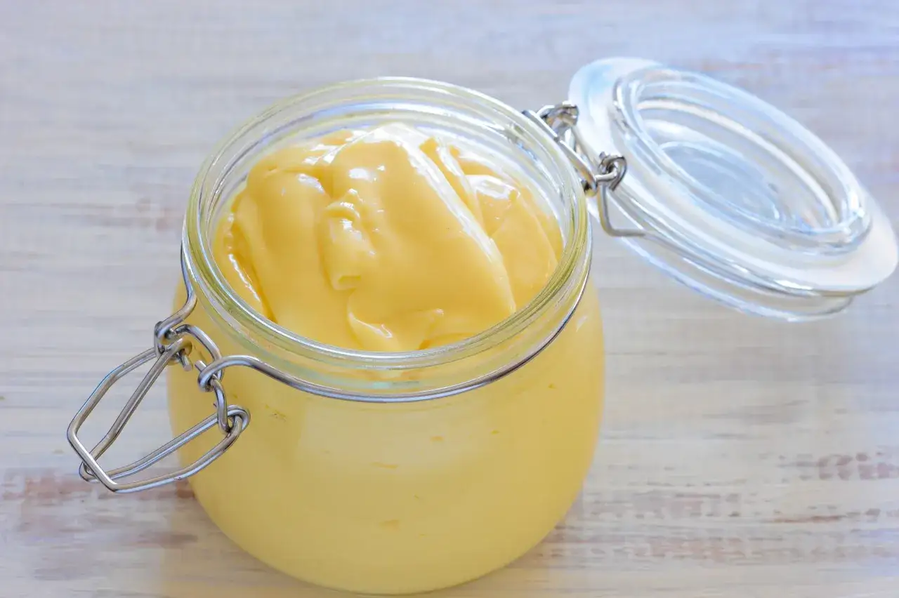 Un pot en verre ouvert révèle une mayonnaise onctueuse, faite maison avec de la mayonnaise huile d'olive.