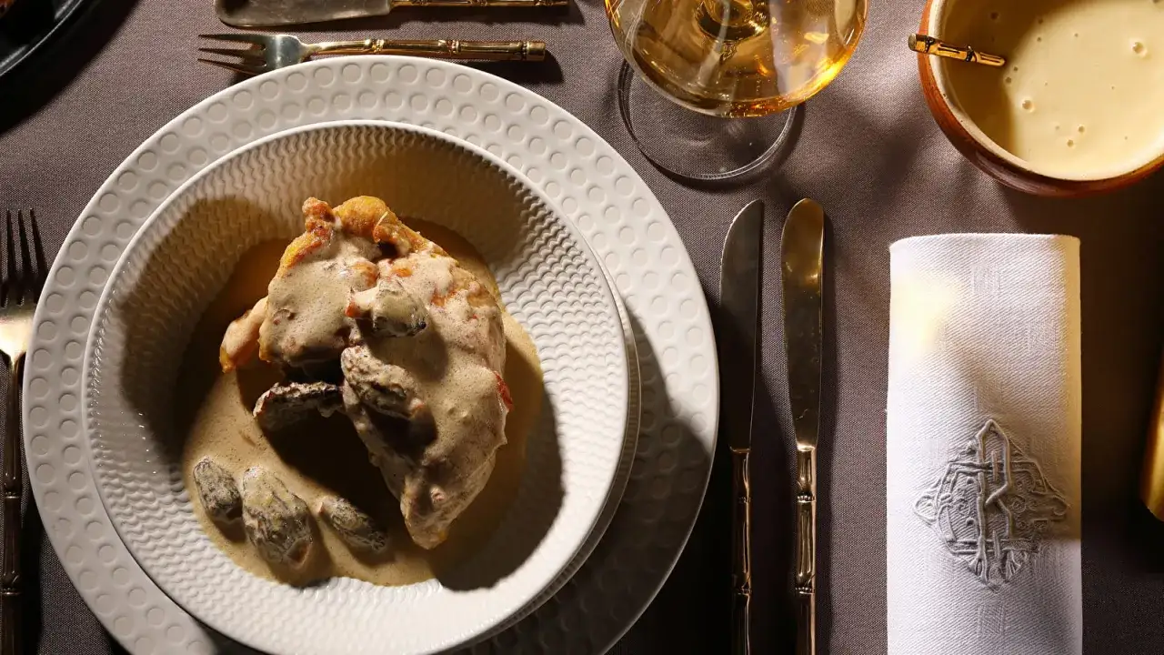 Un plat de poulet au vin jaune, servi dans une assiette creuse, accompagné de morilles et d'une sauce onctueuse. Une table dressée pour un repas raffiné.