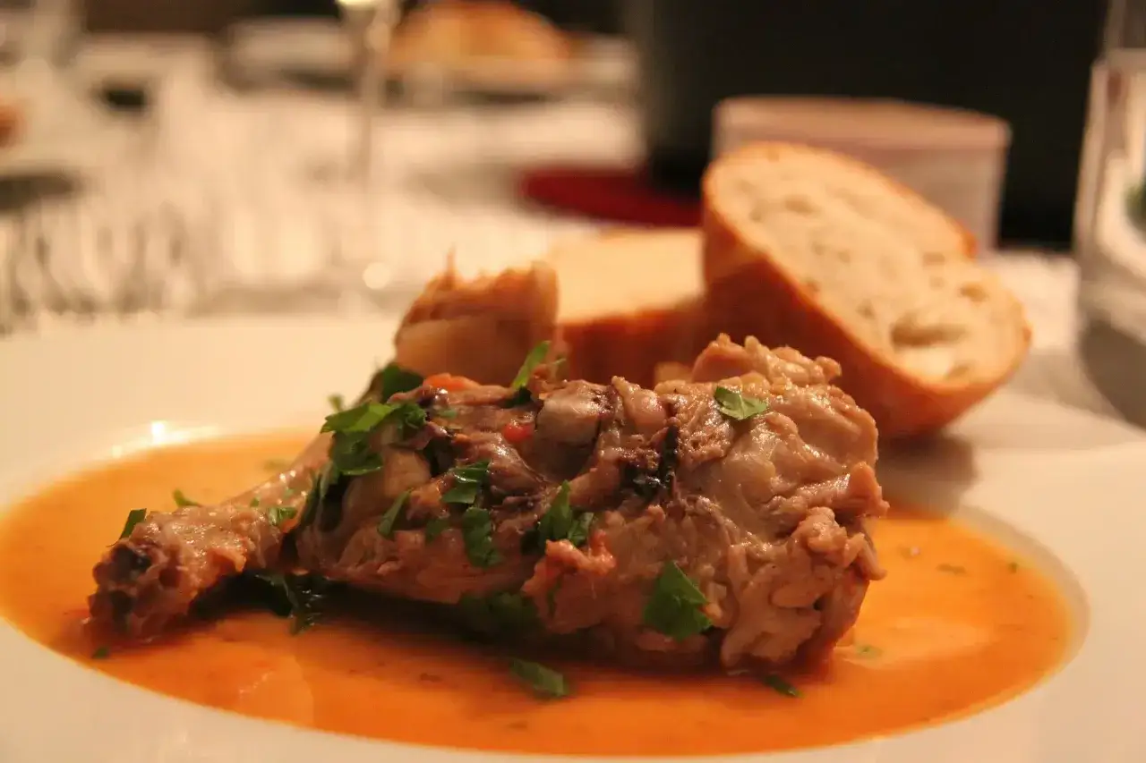 Un plat savoureux d'osso bucco, garni de persil frais, servi avec du pain croustillant. Quel vin avec un osso bucco ? Un rouge corsé serait parfait.