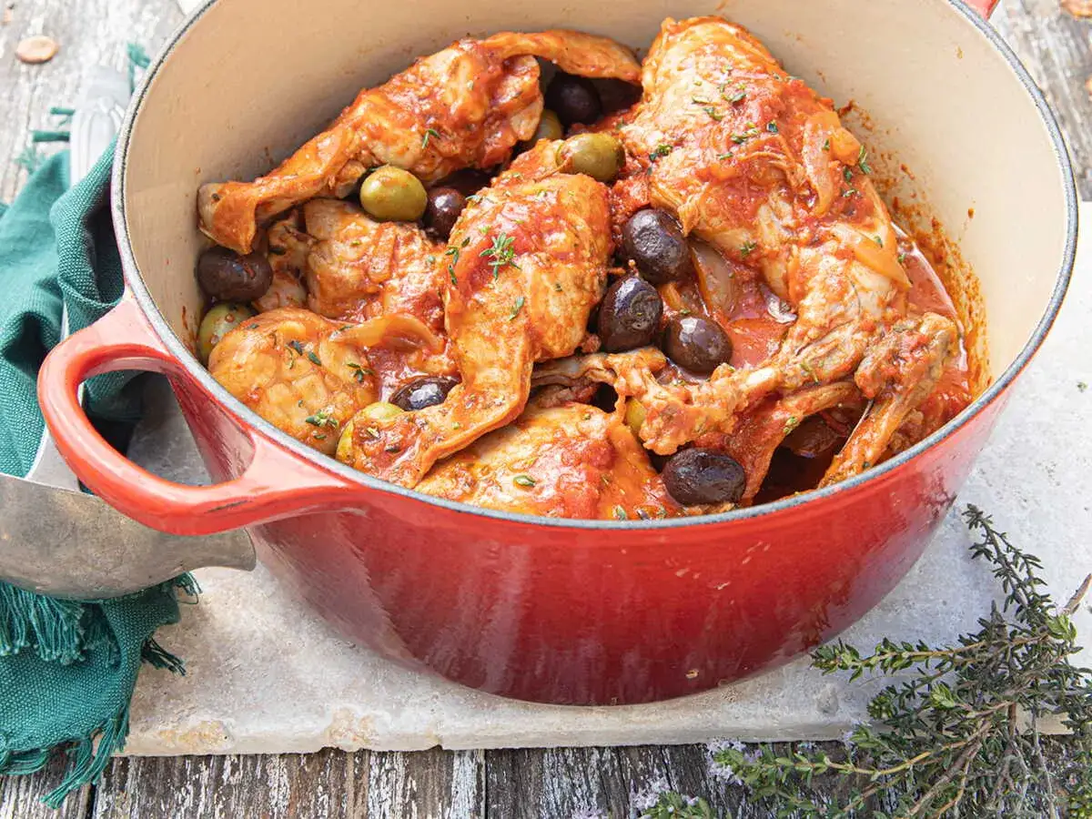 Un plat mijoté de lapin aux olives, baignant dans une sauce tomate savoureuse, garni de thym frais.