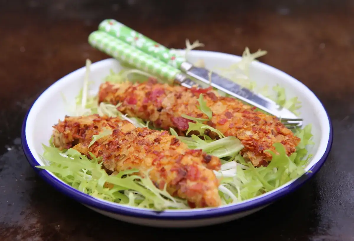 Trois aiguillettes de poulet pané croustillantes, servies sur un lit de salade verte croquante. Des couverts à motifs verts sont posés sur le plat.