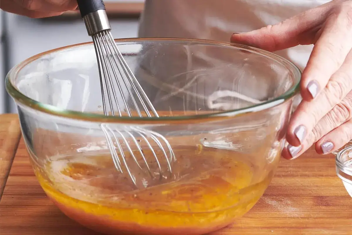 Pr&eacute;paration d'une recette vinaigrette moutarde. Un fouet m&eacute;lange des ingr&eacute;dients dans un bol en verre.