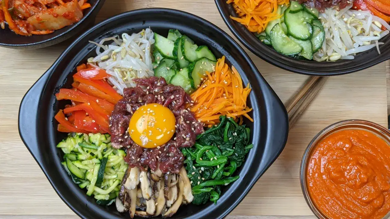 Un plat coloré de bibimbap recette avec bœuf cru, œuf, légumes frais et sauce piquante.
