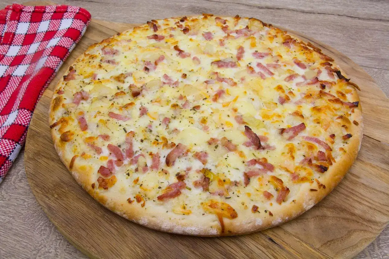 Une délicieuse pizza savoyarde, garnie de lardons et de fromage fondant, prête à être dégustée sur une planche en bois.