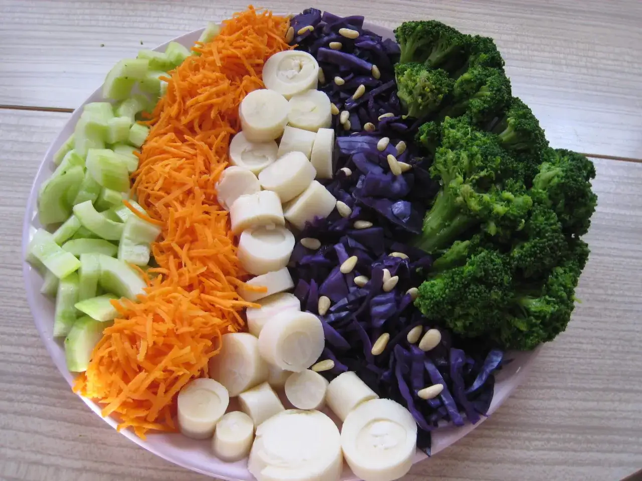 Une assiette colorée de salade de crudités : concombre, carottes râpées, cœur de palmier, chou rouge et brocolis.