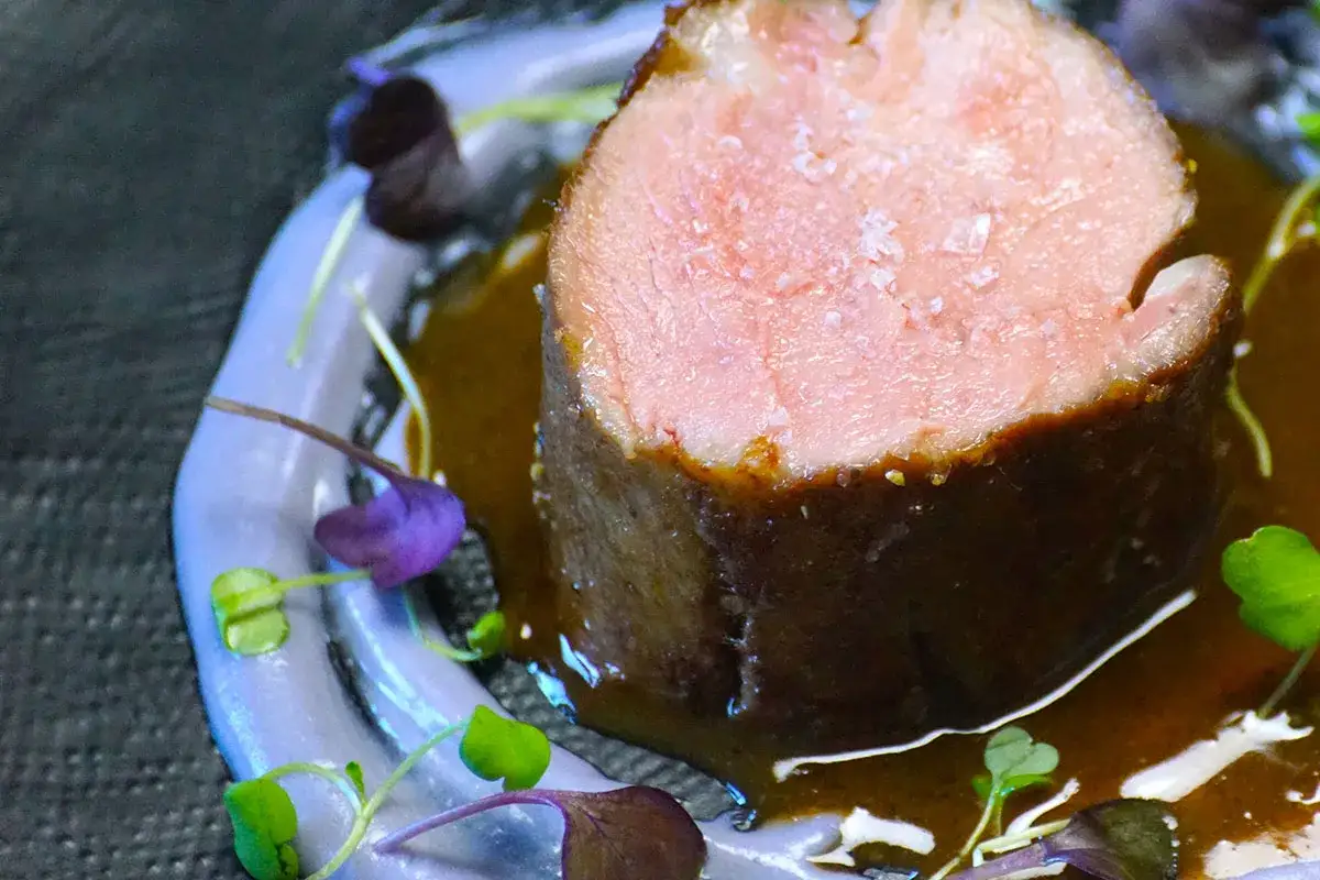 Un morceau de pluma de porc recette, tendre et juteux, nappé d'une sauce brune et garni de pousses pourpres et vertes.