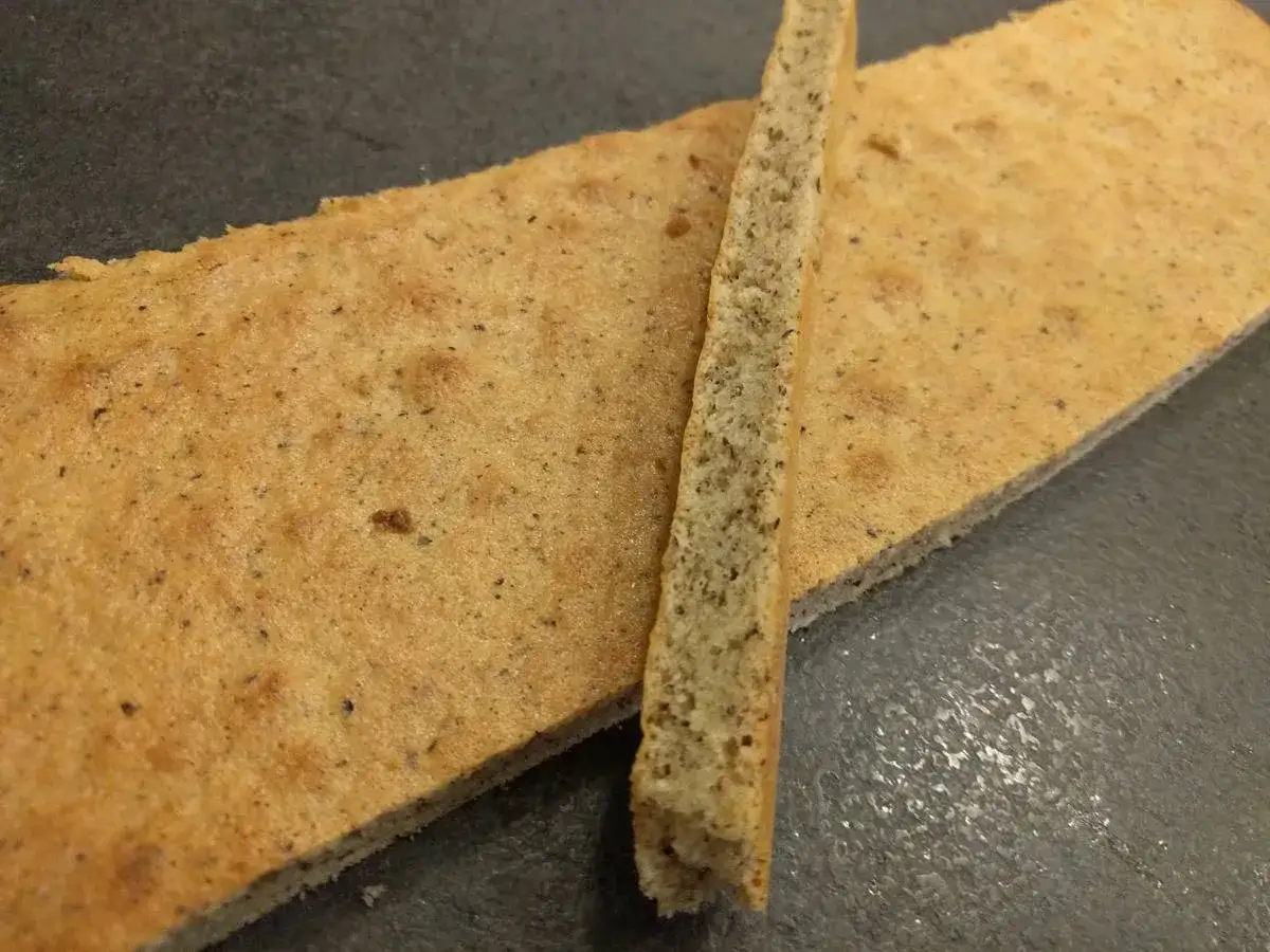 Deux fines tranches de biscuit joconde, l'une posée sur l'autre, sur fond sombre.