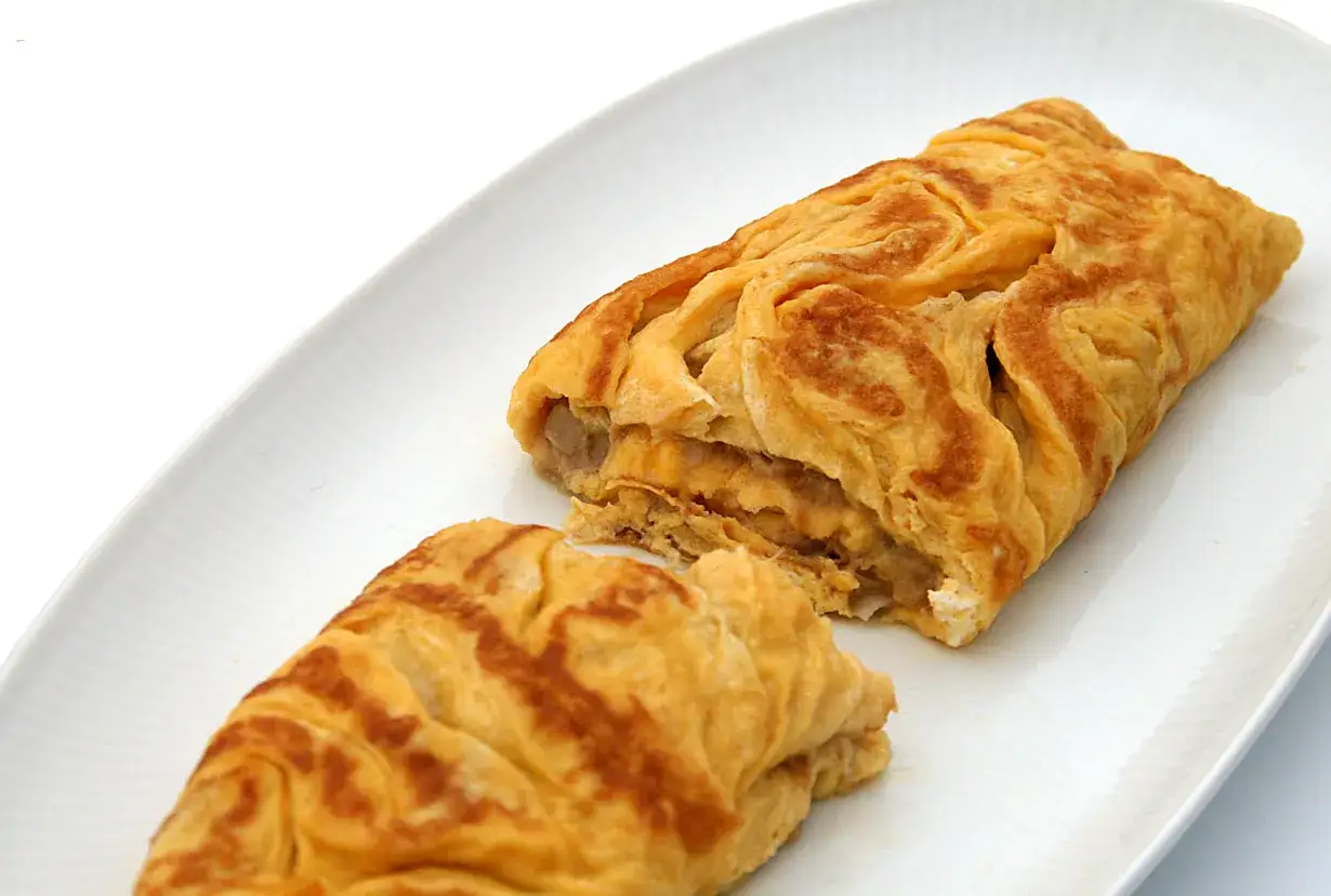 Une omelette au thon, dorée et moelleuse, coupée en deux sur une assiette blanche.